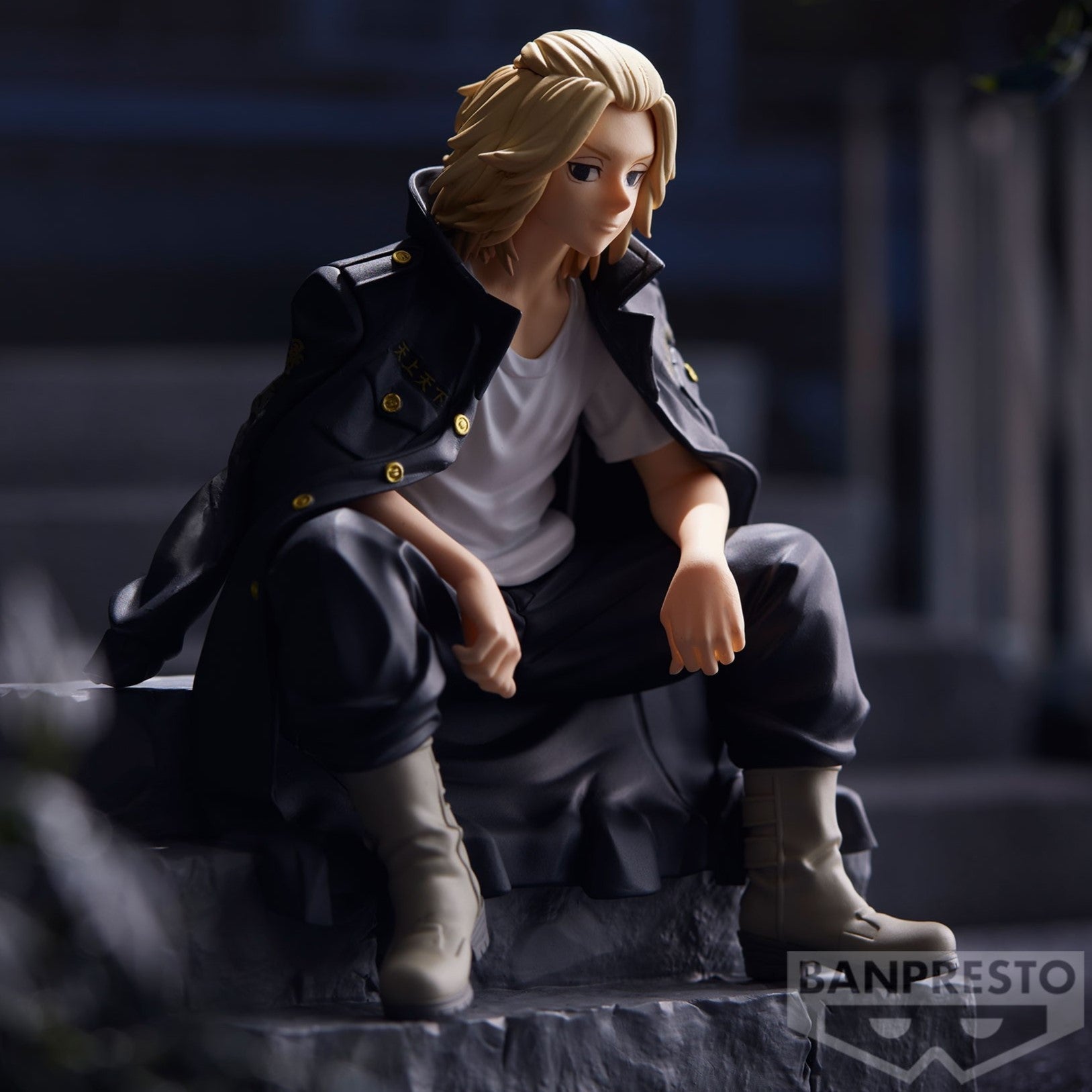 Vue 3/4 de face à mi-distance de la figurine de Manjiro Sano de Tokyo Revengers en manteau noir, assis et pensif.