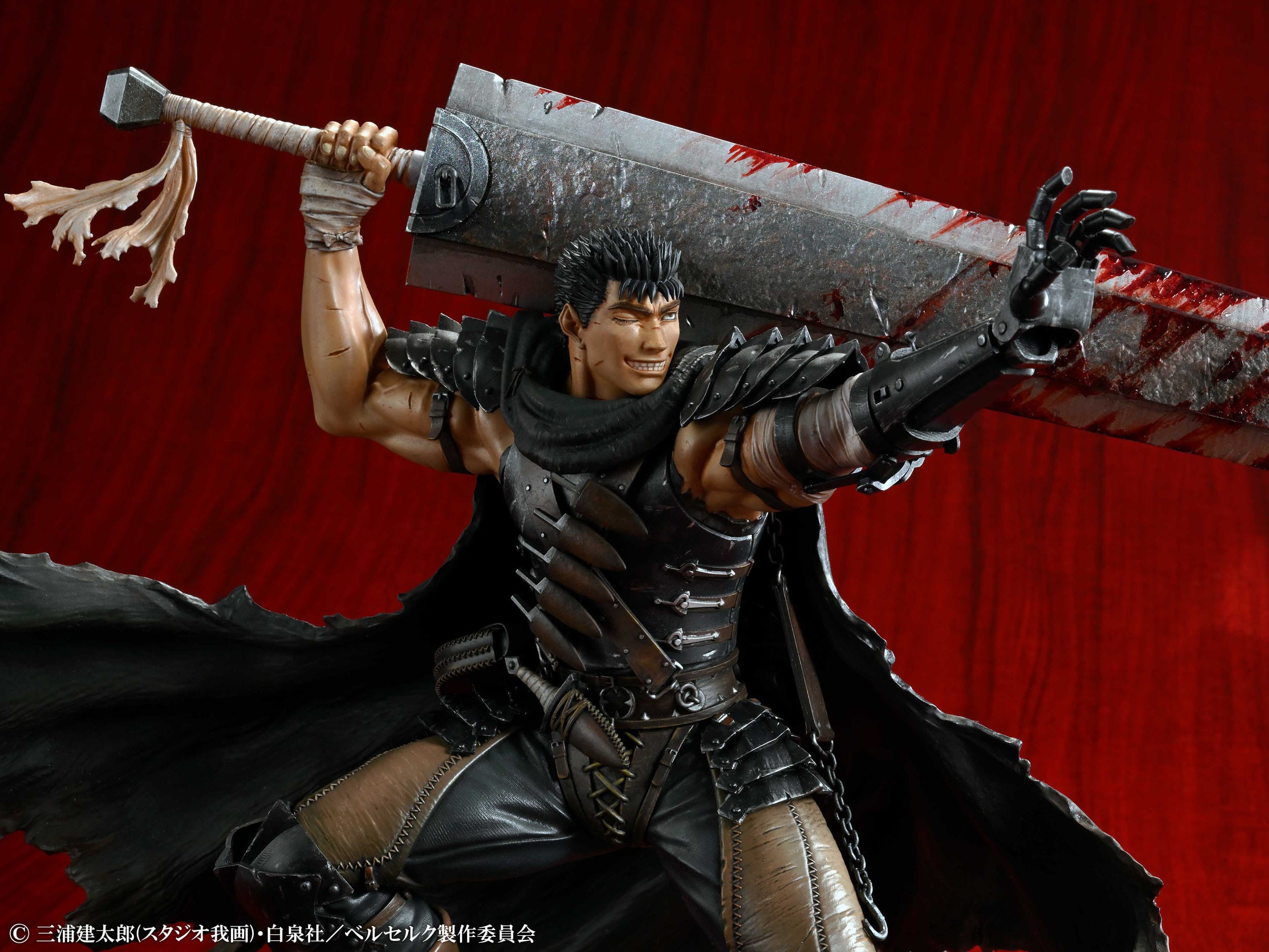 Vue 3/4 de face à mi-distance de la figurine de Guts de Berserk en armure noire avec une cape, tenant une épée ensanglantée.