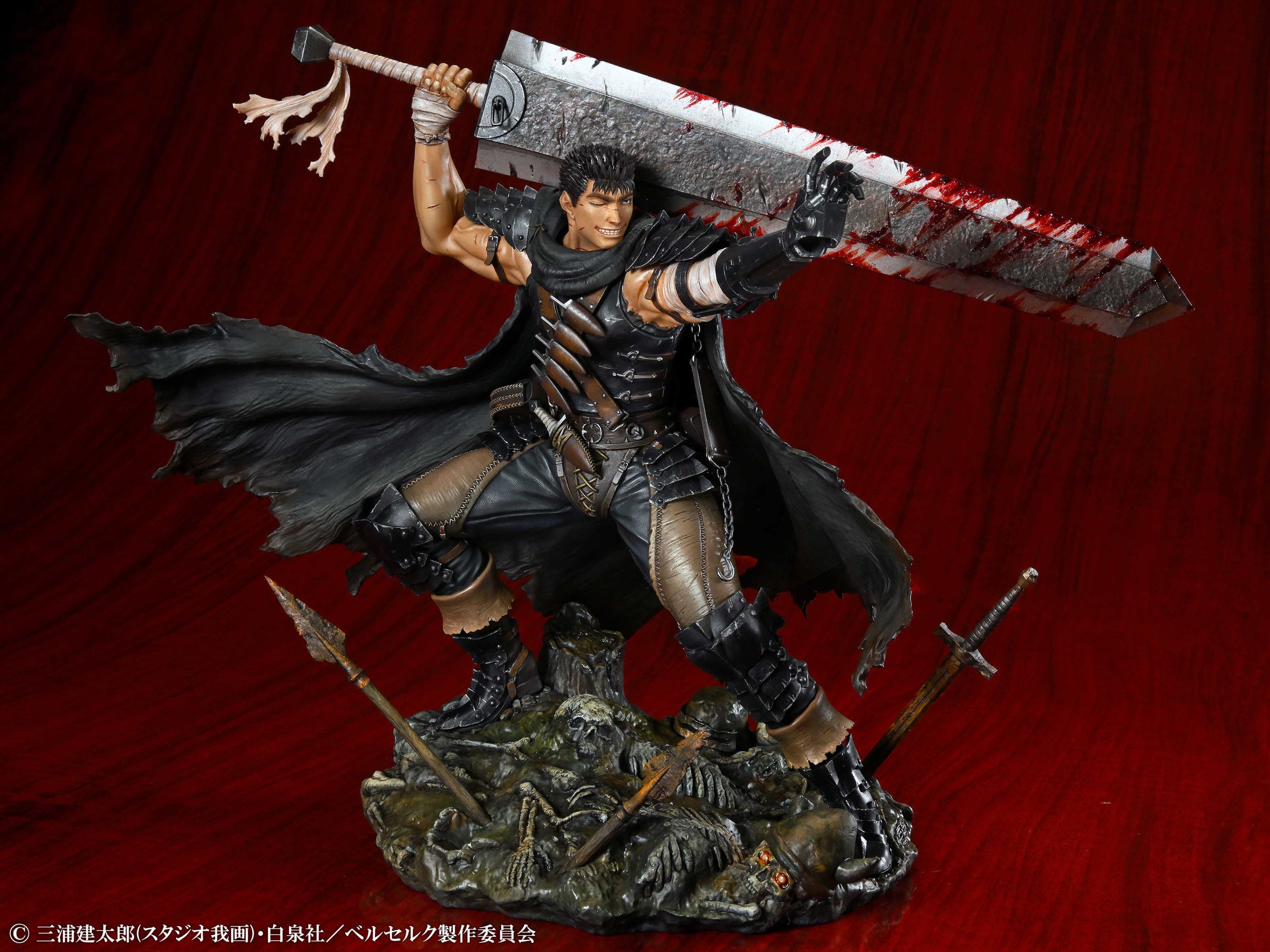 Vue 3/4 de face à mi-distance de la figurine de Guts de Berserk, en tenue sombre avec une grande cape, tenant l'épée Dragon Slayer.