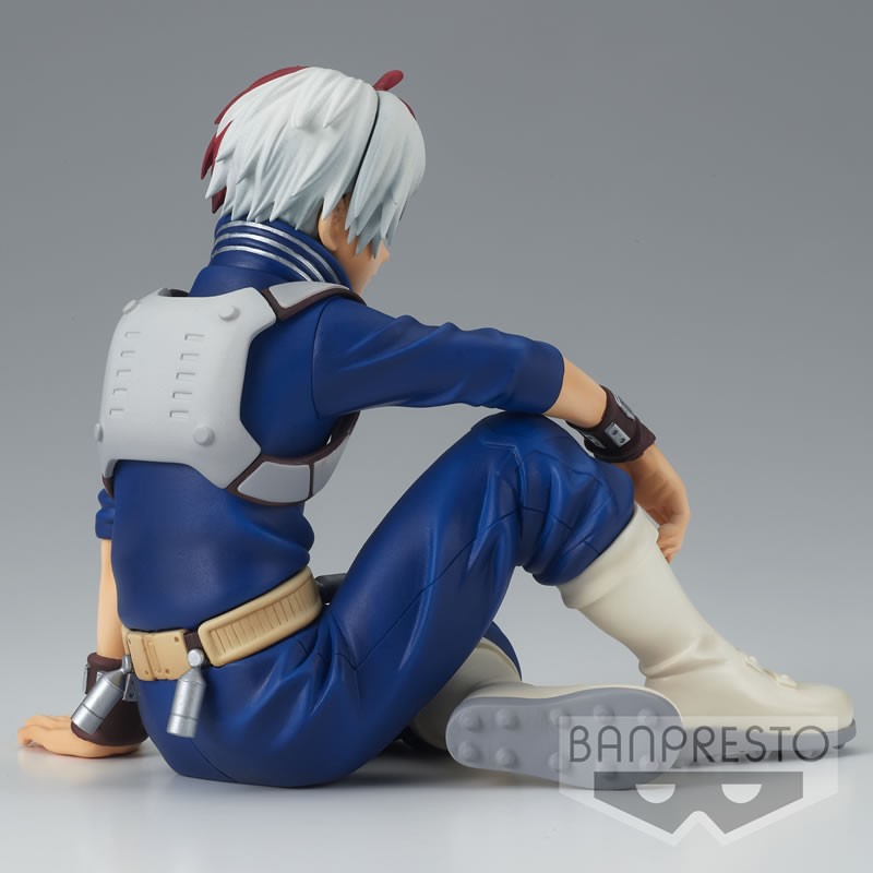 Vue 3/4 de dos à mi-distance de la figurine de Shoto Todoroki de My Hero Academia en combinaison bleue avec gilet d'armure blanc, assis, regardant vers le bas.