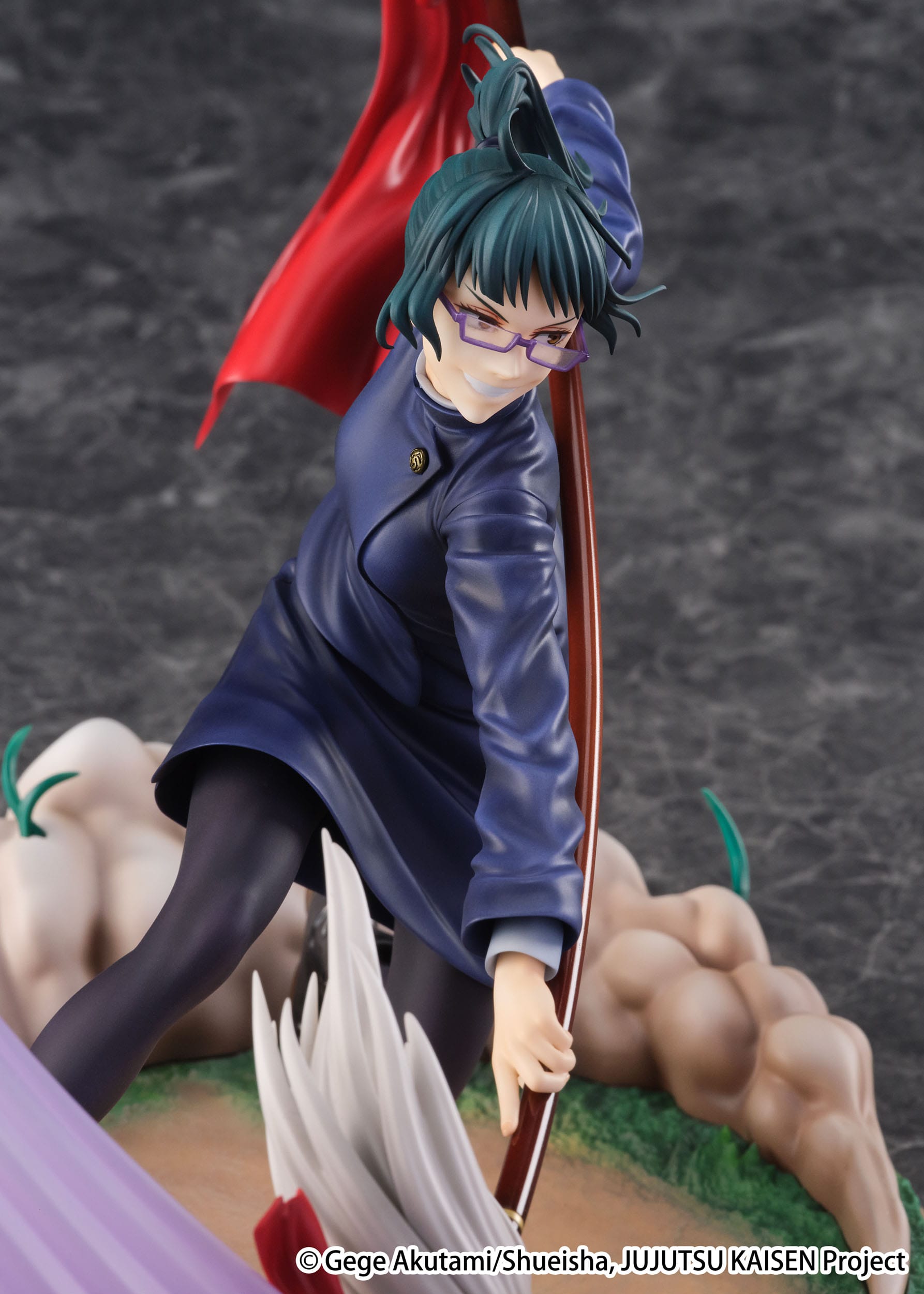 Figurine Maki Zenin de la série Jujutsu Kaisen en manteau bleu foncé, en posture dynamique avec expression intense, tenant un bâton avec un drapeau rouge. Vue de face à mi-distance.