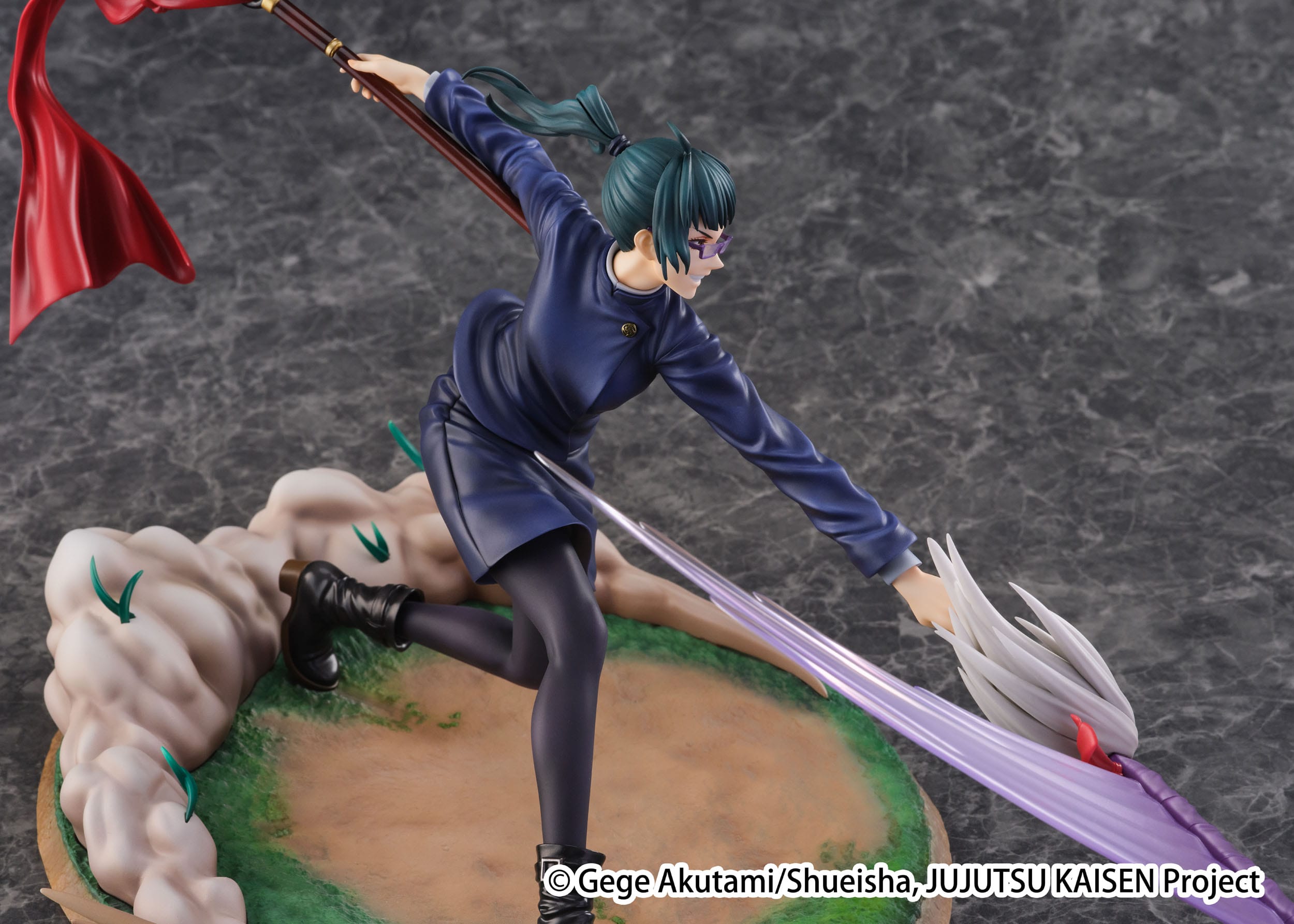 Figurine Maki Zenin de la série Jujutsu Kaisen en uniforme bleu foncé, en posture dynamique avec expression déterminée, tenant une arme courbée avec un ruban rouge. Vue de face à mi-distance.