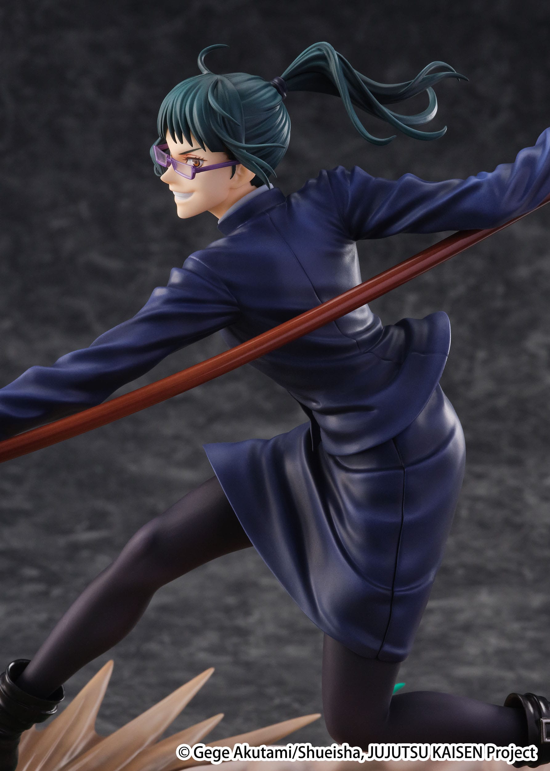 Figurine Maki Zenin de la série Jujutsu Kaisen en uniforme bleu, en posture dynamique avec expression confiante, tenant un long bâton. Vue de face à mi-distance.