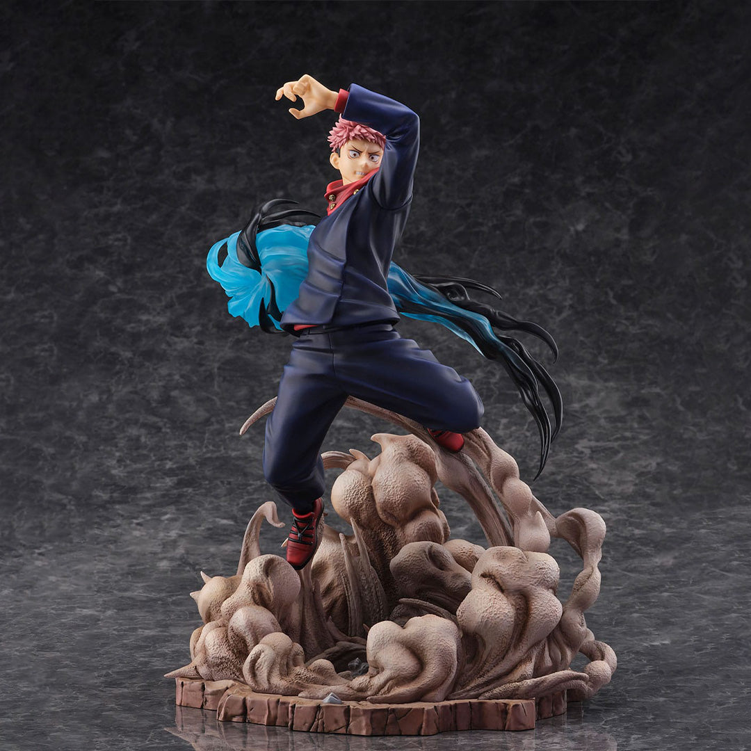 Figurine Yuji Itadori de la série Jujutsu Kaisen en tenue bleu foncé, en posture dynamique avec expression déterminée, bras levé, entouré d'éléments tourbillonnants. Vue de face à mi-distance.