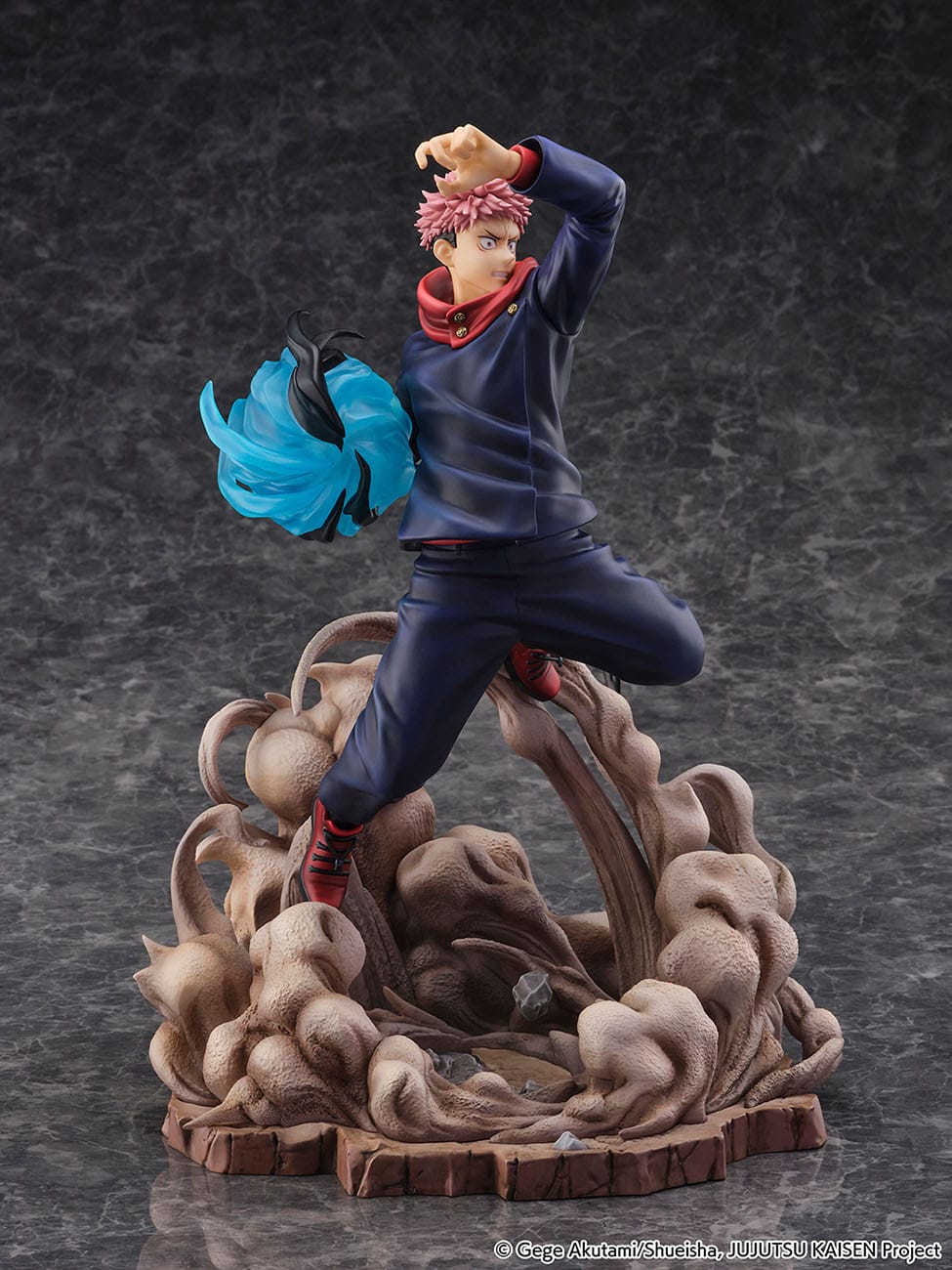 Figurine Yuji Itadori de la série Jujutsu Kaisen en tenue bleu foncé avec accents rouges, en posture dynamique avec expression déterminée, main levée et aura tourbillonnante. Vue 3/4 à mi-distance.