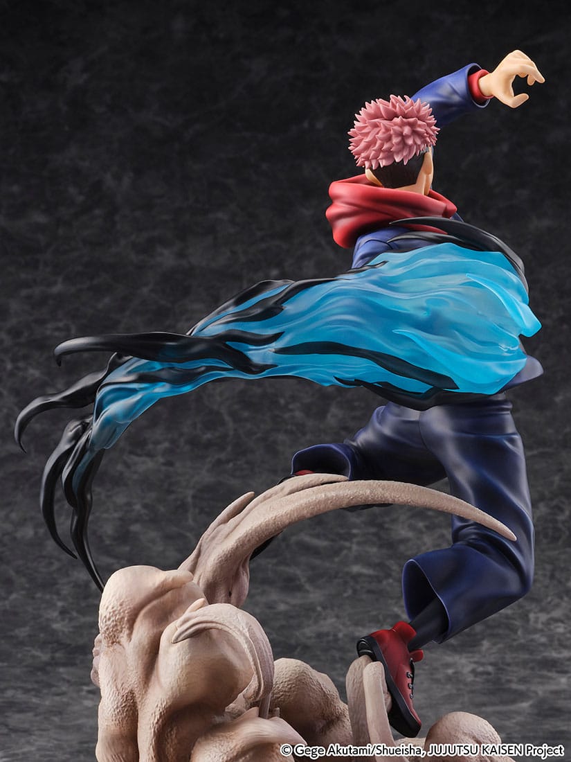 Figurine Yuji Itadori de la série Jujutsu Kaisen en tenue bleu foncé avec écharpe rouge, en posture d'action avec expression déterminée, émanant une énergie bleue et noire de son bras. Vue de face à mi-distance.
