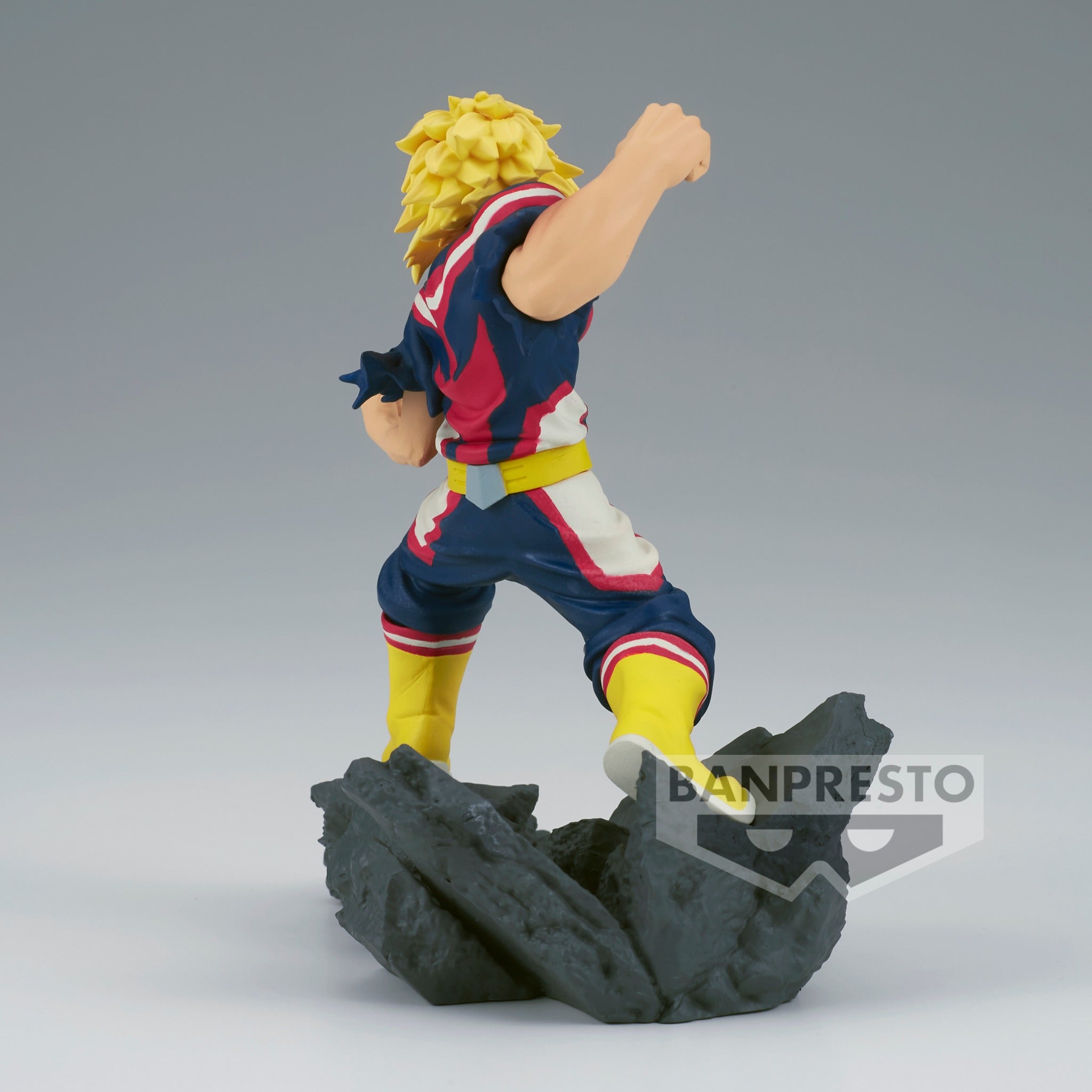 Vue 3/4 arrière à mi-distance de la figurine  d'All Might de My Hero Academia en costume de super-héros, avec un bras levé.