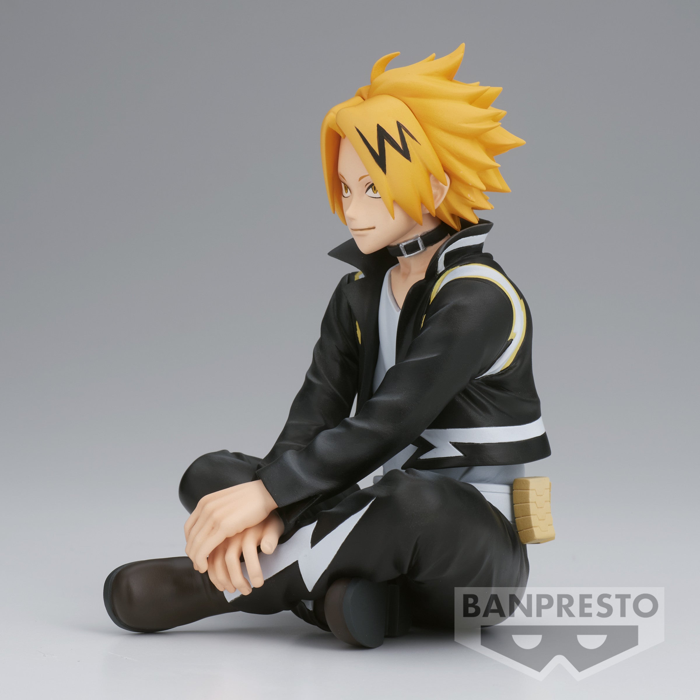 Vue de profil à mi-distance de la figurine de Denki Kaminari de My Hero Academia, assis avec un gilet noir et un motif en zigzag blanc, portant un choker et un accessoire en boîte à côté.