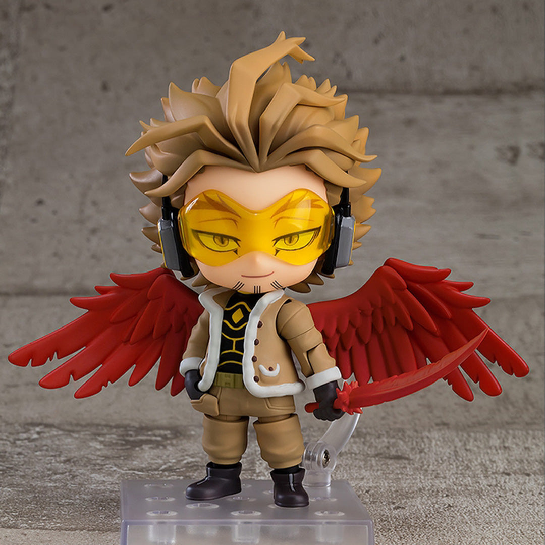 Vue 3/4 de face à mi-distance de la figurine Nendoroid de Hawks de My Hero Academia en tenue beige et blanche, avec des ailes rouges et tenant une épée.