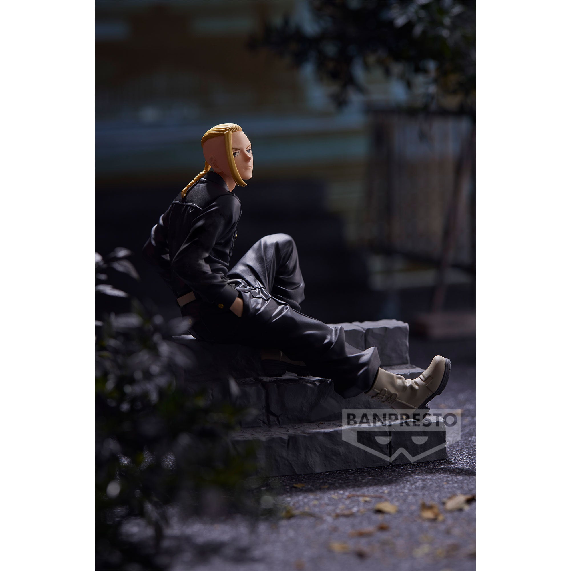 Vue de profil à mi-distance de la figurine de Draken de Tokyo Revengers en tenue noire, assis sur une marche en pierre.