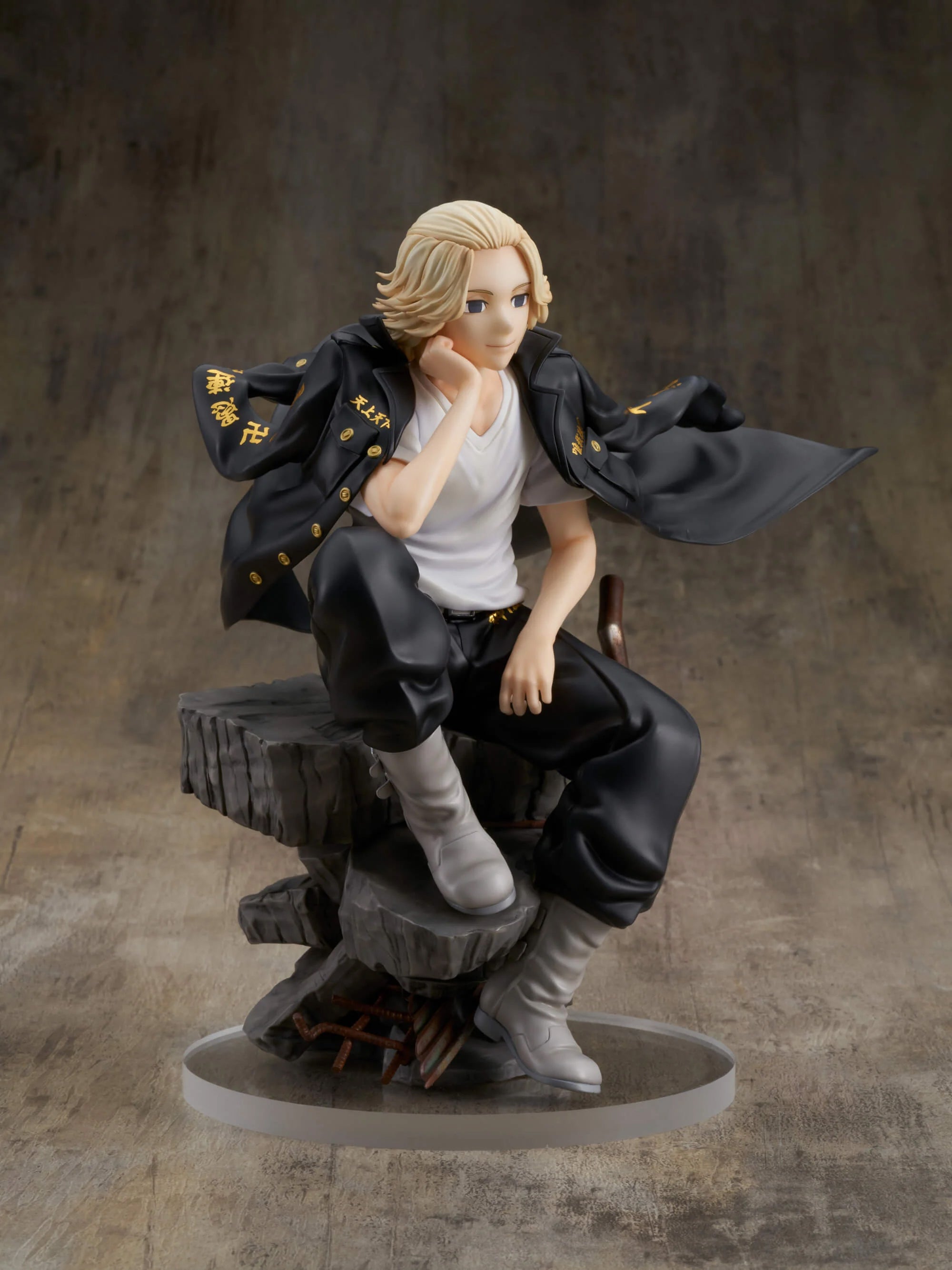 Vue 3/4 de face à mi-distance de la figurine de Manjiro Sano de Tokyo Revengers en manteau noir avec t-shirt blanc, assis sur un socle en roche stylisé.