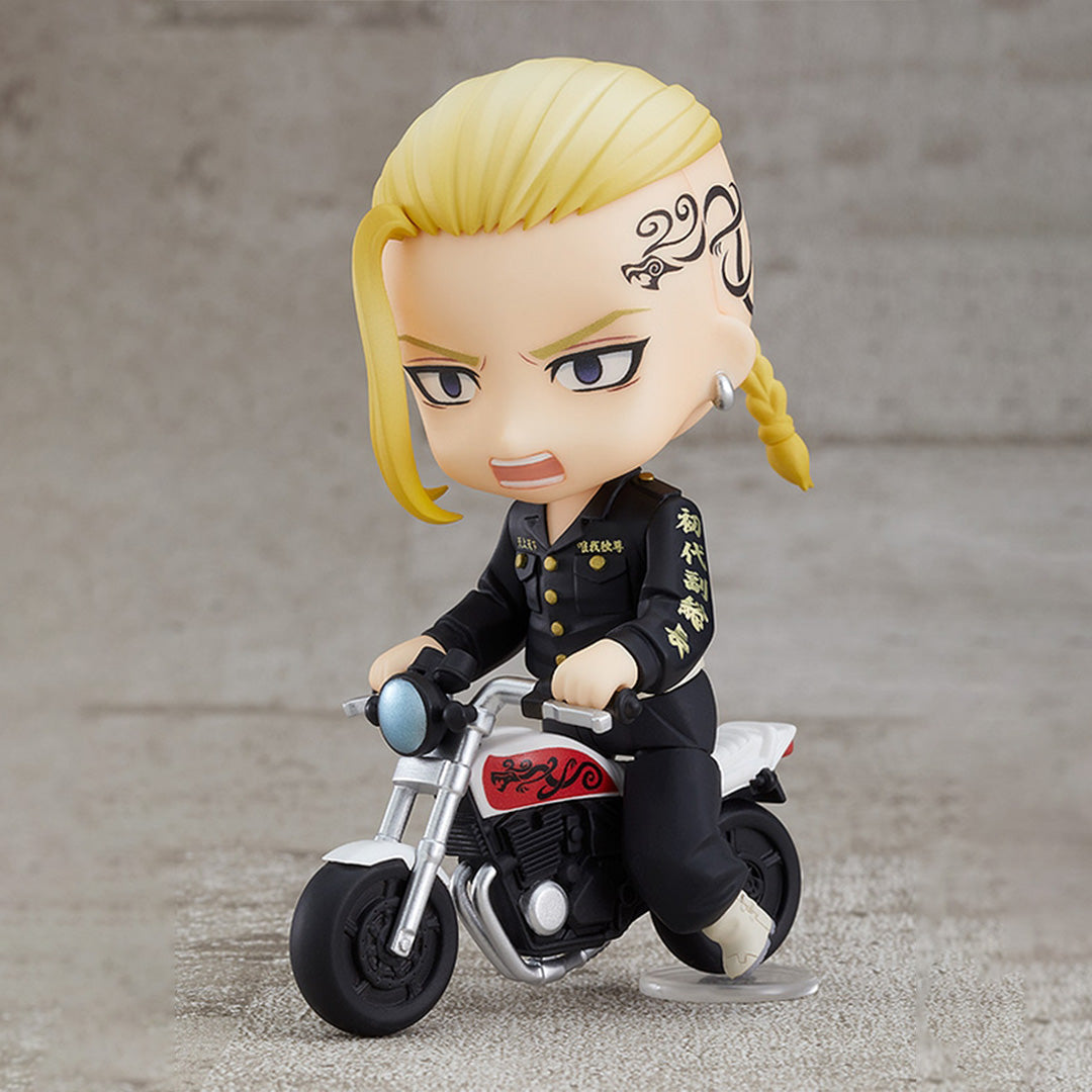 Vue 3/4 de face en plan rapproché de la figurine de Ken Ryuguji (Draken) de Tokyo Revengers en uniforme noir avec des boutons dorés, tenant fermement les poignées de sa moto miniature.
