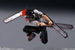 Vue dynamique à mi-distance de la figurine de Denji de Chainsaw Man, en posture accroupie, portant une chemise blanche et des armes en forme de tronçonneuse.