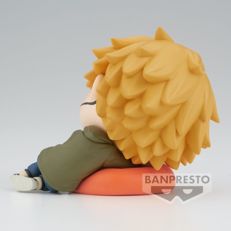 Vue 3/4 arrière en plan moyen de la figurine chibi de Denji de Chainsaw Man, vêtu d'une veste verte, assis sur un coussin orange.