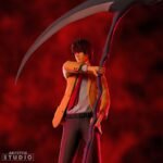 Vue 3/4 de face en plan complet de la figurine de Light Yagami de Death Note en tenue décontractée, tenant une grande faux.