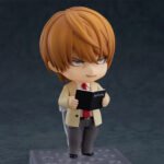 Vue 3/4 de face à mi-distance de la figurine de Light Yagami de Death Note en blazer beige, tenant le Death Note.
