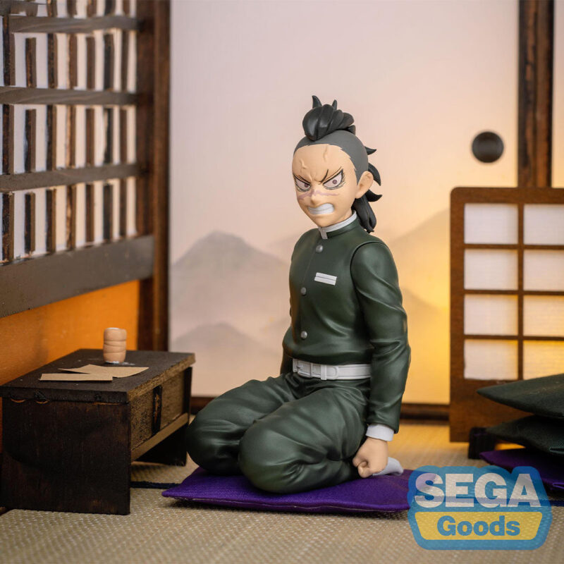 Vue 3/4 à mi-distance de la figurine de Genya Shinazugawa de Demon Slayer en tenue traditionnelle, avec une expression déterminée, à genoux près d'une petite table.