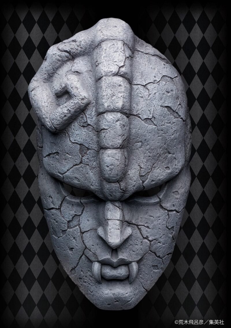 Vue de face en plan rapproché de la Stone Mask de JoJo's Bizarre Adventure: Phantom Blood, avec des fissures et des dents proéminentes.