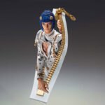 Vue 3/4 de face à mi-distance de la figurine de Bruno Bucciarati de JoJo's Bizarre Adventure en costume blanc à pois noirs, émergeant d'une fermeture éclair.