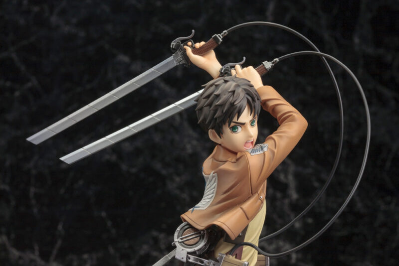 Vue 3/4 de face à mi-distance de la figurine ArtFX J d'Eren Yeager de Shingeki no Kyojin en uniforme militaire, tenant des épées.
