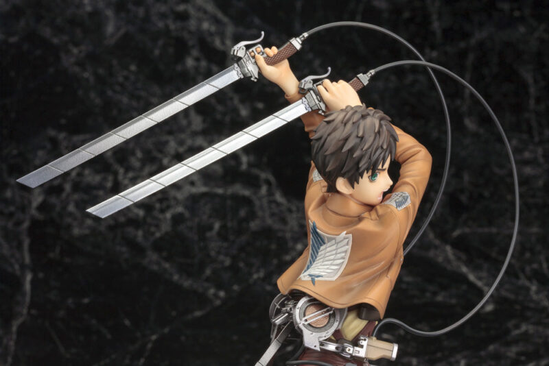 Vue 3/4 de dos à mi-distance de la figurine ARTFX J d'Eren Yeager de Shingeki no Kyojin en uniforme militaire, tenant deux épées.