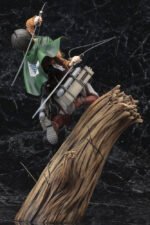 Vue dynamique en plan moyen de la figurine de Levi Ackerman de Shingeki no Kyojin en uniforme de la Survey Corps, tenant des lames.