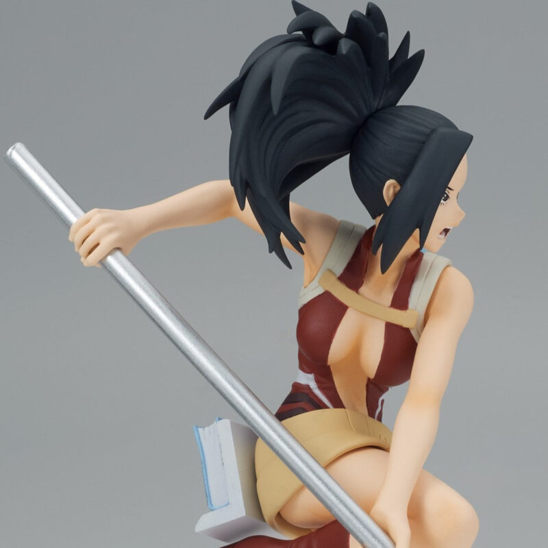 Vue 3/4 de face à mi-distance de la figurine de Momo Yaoyorozu de My Hero Academia en tenue moulante rouge et beige, tenant un pôle argenté.