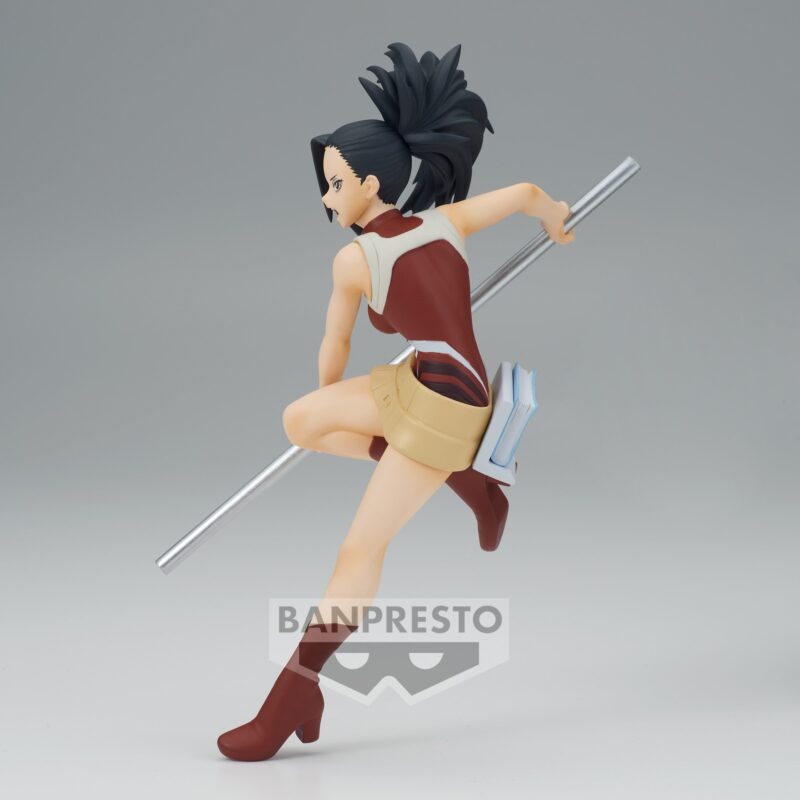 Vue 3/4 arrière à mi-distance de la figurine  de Momo Yaoyorozu de My Hero Academia en tenue rouge et crème, tenant un bâton métallique et un livre.