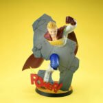 Vue 3/4 de face à mi-distance de la figurine de Mirio Togata de My Hero Academia en costume de héros, en pose dynamique à travers un mur.