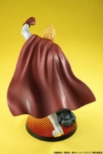 Vue 3/4 arrière en gros plan de la figurine de Mirio Togata de My Hero Academia en costume de héros avec une cape rouge, bras levé.