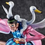 Figurine de Bon Clay avec une pose dynamique, portant une jupe bleue rayée, une ceinture rouge et une longue cape rose ornée d'ailes et de têtes de cygne, fabriquée par MEGAHOUSE.